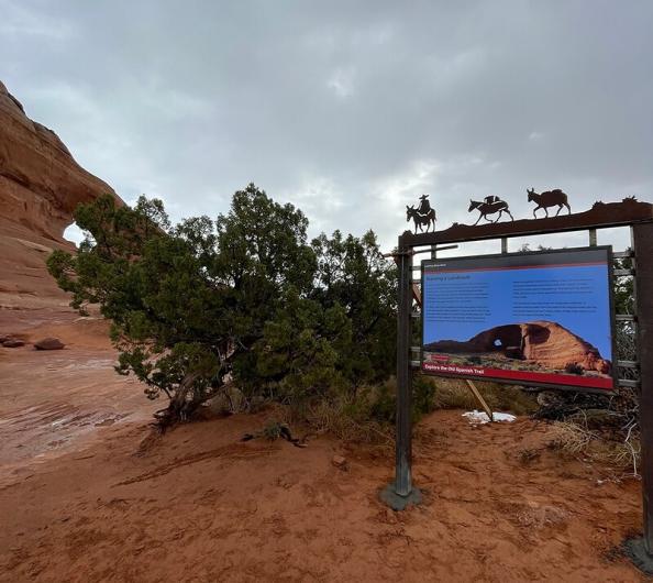 Informational signs in from of an arch rock formation.