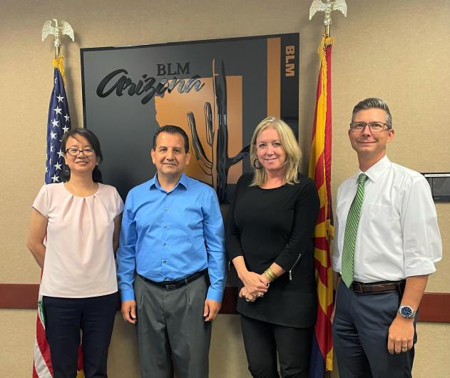 A group of BLM Arizona leadership and Hebin Lin stand for a photo in front of two flags.