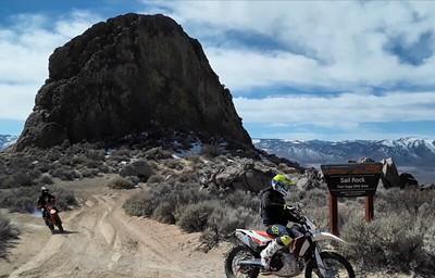 OHVs ride in front of  a large rock  in the high desert.