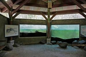 Photo shows two large windows looking into a streambed with interpretive signs on either side of the windows, a roof above, and large boulders and benches to sit on while you watch the fiish.