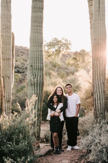 Three people pose for a picture in front of cacti.
