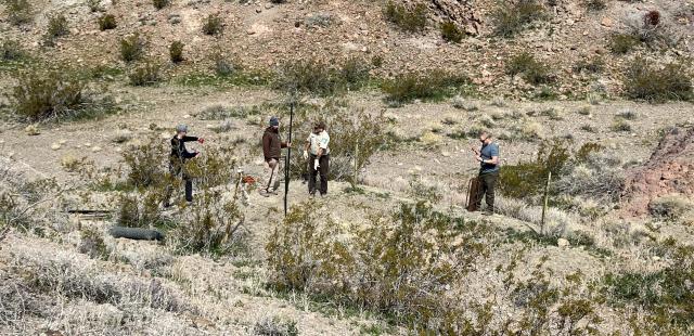 Four people examine a shaft in the desert