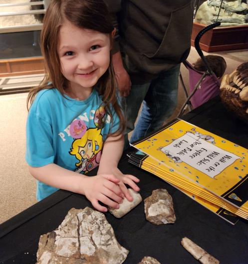 Smiling young girl feels fossils at a table covered in black