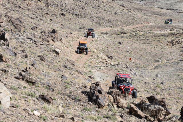 A caravan of OHVs and ATVs on a rocky hillside switchback.