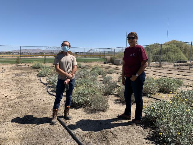 two students pose in front of a garden bed.