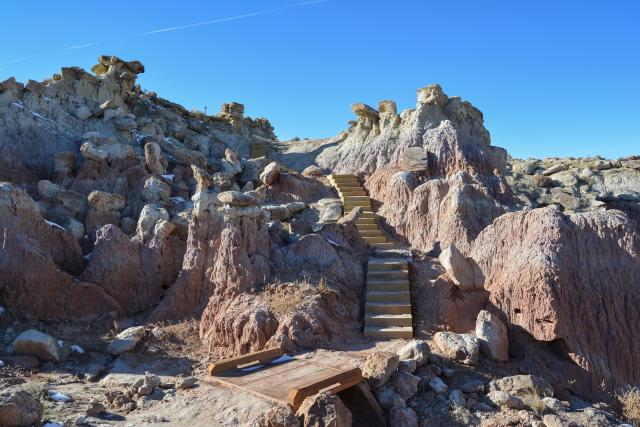 A flight of wooden steps that blends in with the surrounding landscape leads up and into badlands features.