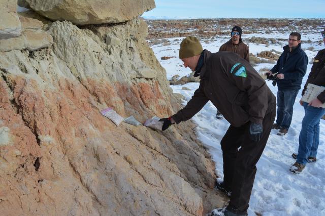 A person wearing a jacket with a BLM logo examples bags of gravel, comparing the colors with the rock they are laid on.