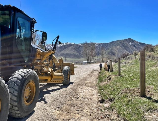 Workers use shovels and other road maintenance equipment on a gravel road.