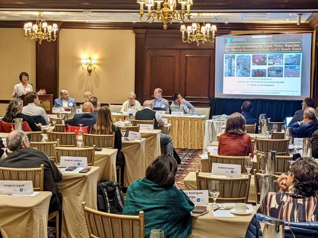 People sitting a various tables looking at a large screen while listening to a presenter