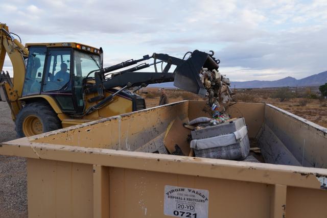 A front end loader fills a dumpster with a couch and other trash.