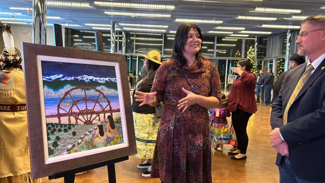A woman with long dark hair gesturing towards art while facing a man in a suit