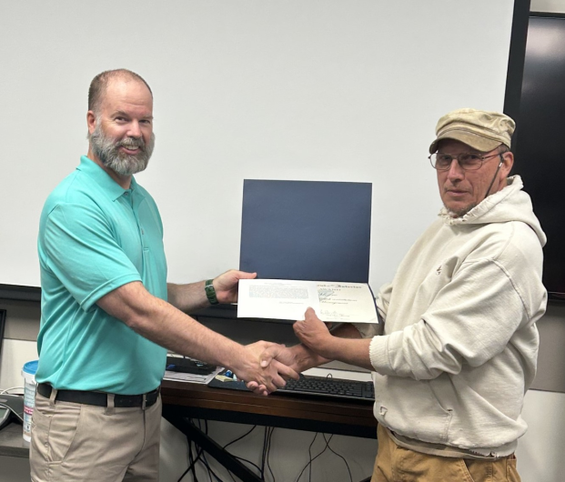 One man hands another an award during presentation.