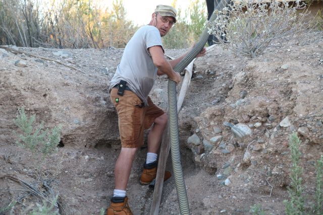 Maintenance worker climbs down embankment while adjusting hoses for vault toilet pumping.r 