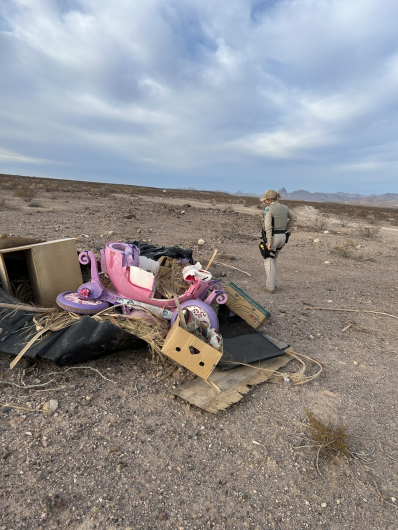 Dumped trash in the foreground with desert scenery while ranger surveys it.