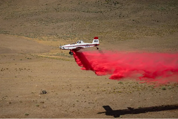 A small white plane in flight with a large plume of red falling from it