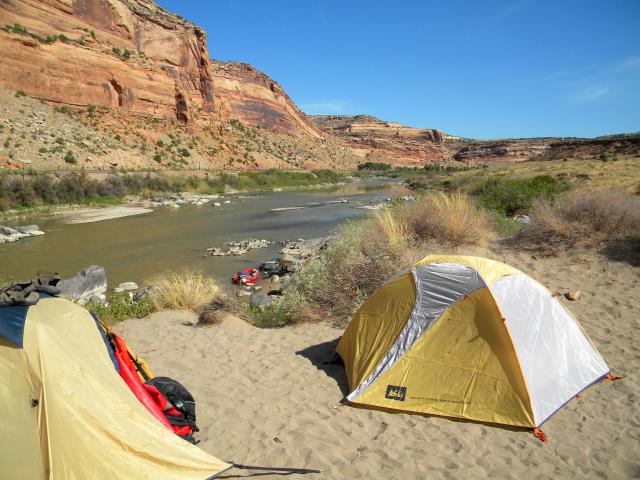 Tents set up at camp site along the Colorado River with rock formations in background