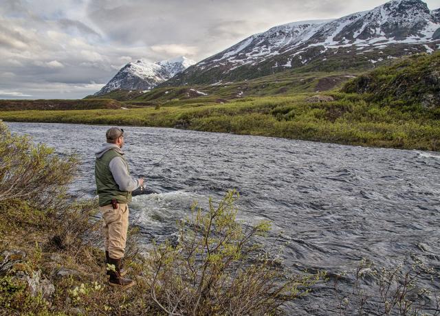 Man fishing on a river with snow-capped mountains in the background
