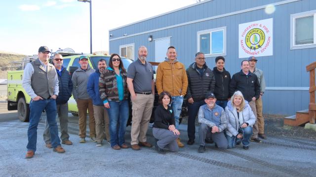 Group of 14 Native American and Caucasian people pose next to a parked green yellow truck.