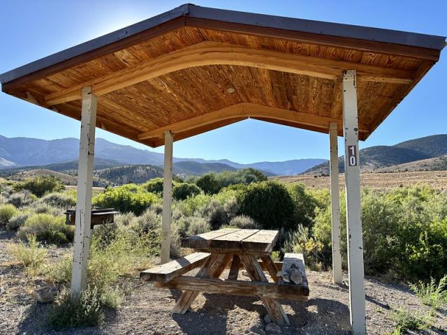 Picnice table under a shade structure overlooking a sunny vista.