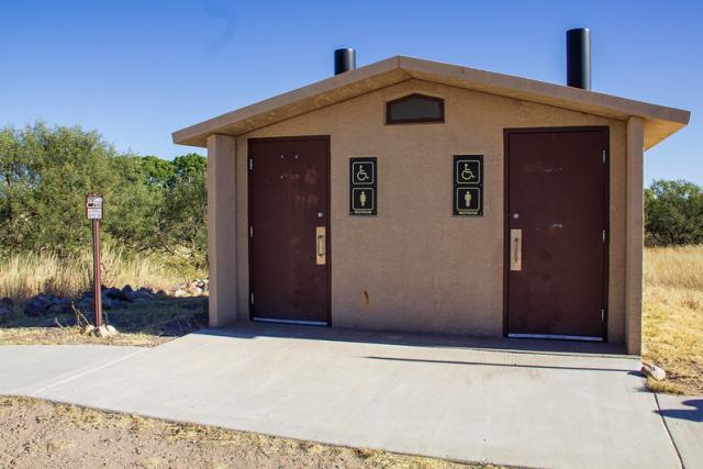 A photo showing a double vault toilet in a brown building, sitting on a large concrete slab.