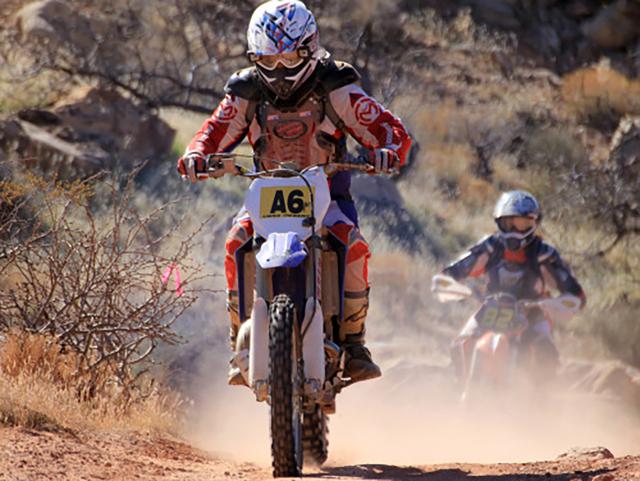 A person in full motor bike racing gear on a motorcycle driving through the desert