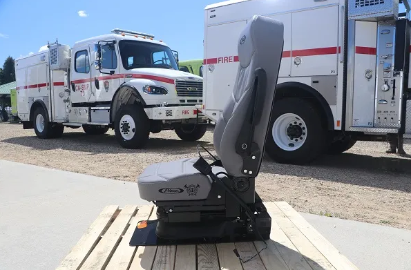 A car seat sits on a pallet outdoors with fire engines in the background