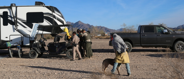 A person with a dog is in the foreground, while several Rangers are standing next to an RV.