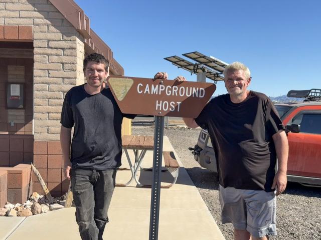 Two men stand near a campground host sign