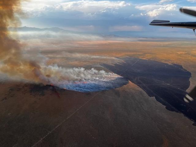 A wide field of view of brown landscape with large cloud of smoke rising from the ground.