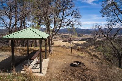 A shade ramada and fire pit overlooking a dry grass valley