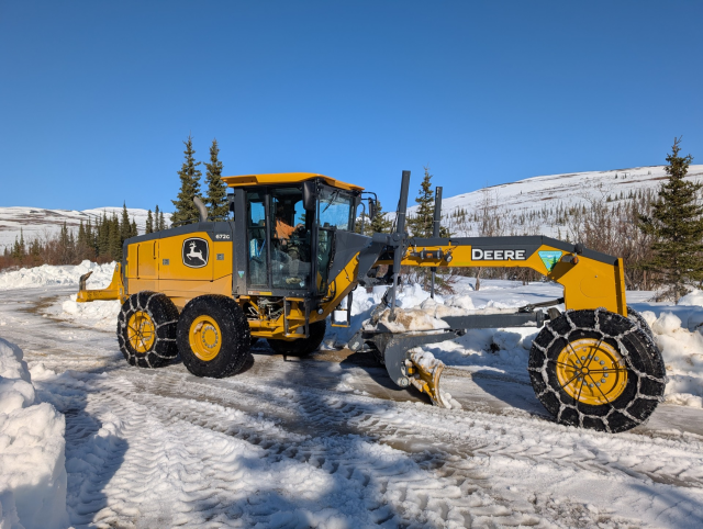 Image of a yellow grader clearing snow from the road. 