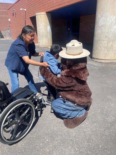 A child stands from a wheelchair to give a hug to Smokey Bear