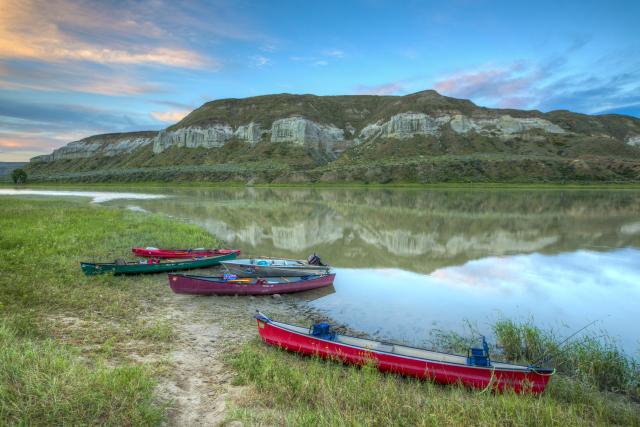 Five canoes are laid out on the bank of a river.