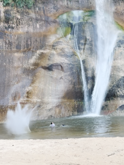 Rockfall splash near two swimmers in a pond under a waterfall.