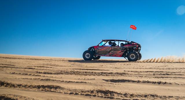 An off-road vehicle drives across a sandy desert area.