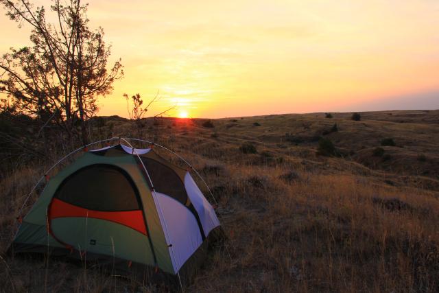 A tent sits on a valley floor as the sun sets in the distance.