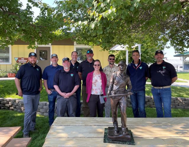 Smiling group of people pose behind a metal statue of a firefighter