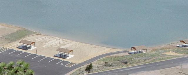 A photo showing four picnic shelters on the lakeshore. Two picnic shelters are next to eight paved, striped parking spaces with accessible parking. An asphalt path leads from the parking area to a third picnic shelter.