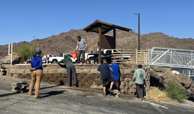 Workers stand next to retaining wall partially repaired.