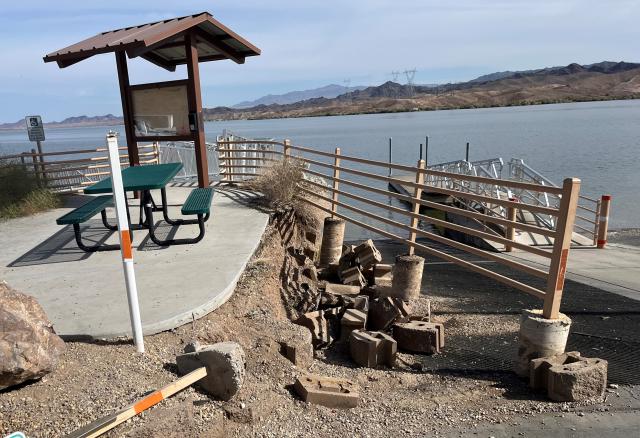 A handrail hanging over a collapsed retaining wall with a lake in the background.