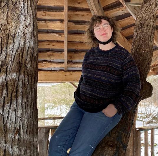 woman poses in a pavilion leaning against a wooden post
