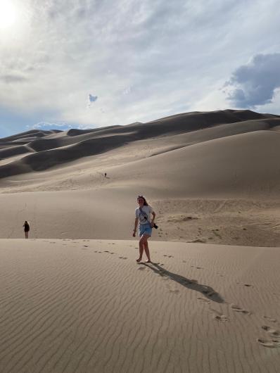 a woman poses for a picture she is standing in the sand dunes.