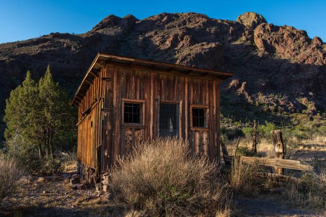 A wooden building in front of a rocky hill.