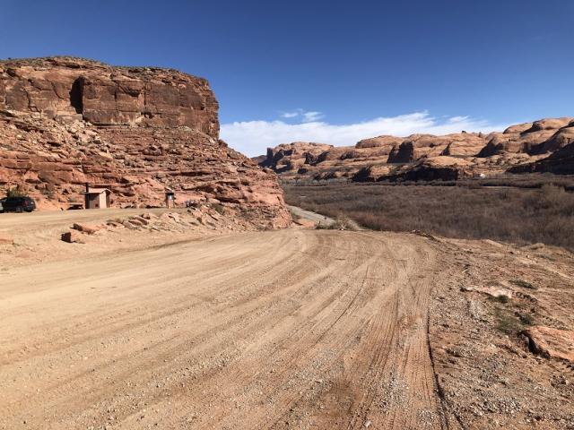 A smooth dirt road along red rock outcroppings and mesas.