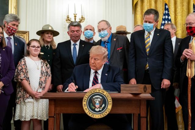 President Trump seated and signing a document as people stand behind him watching.