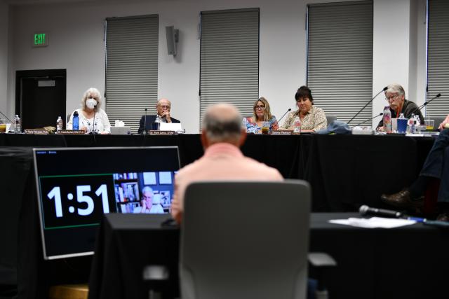 A person sitting at a table facing a panel of people on a stage. 