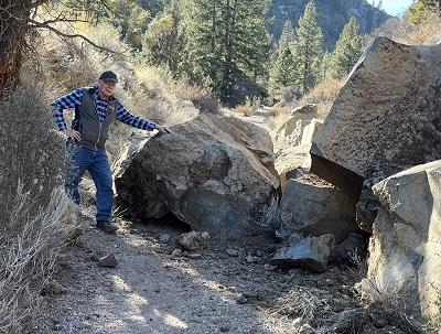 A man stands next to large boulder blocking the trail.