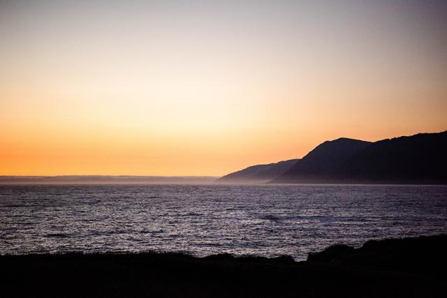 orange sunsetting on dark mountains near the ocean