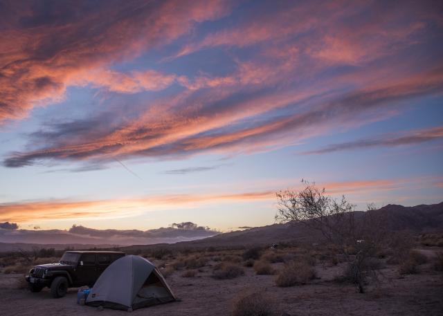 pink and orange skies over a jeep and tent in the desert