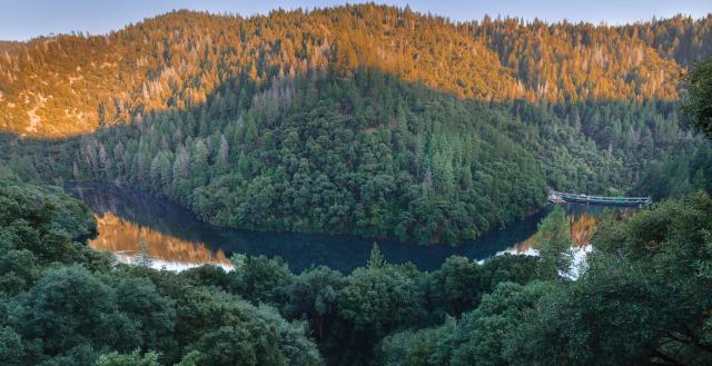 winding river below a settp hill of trees